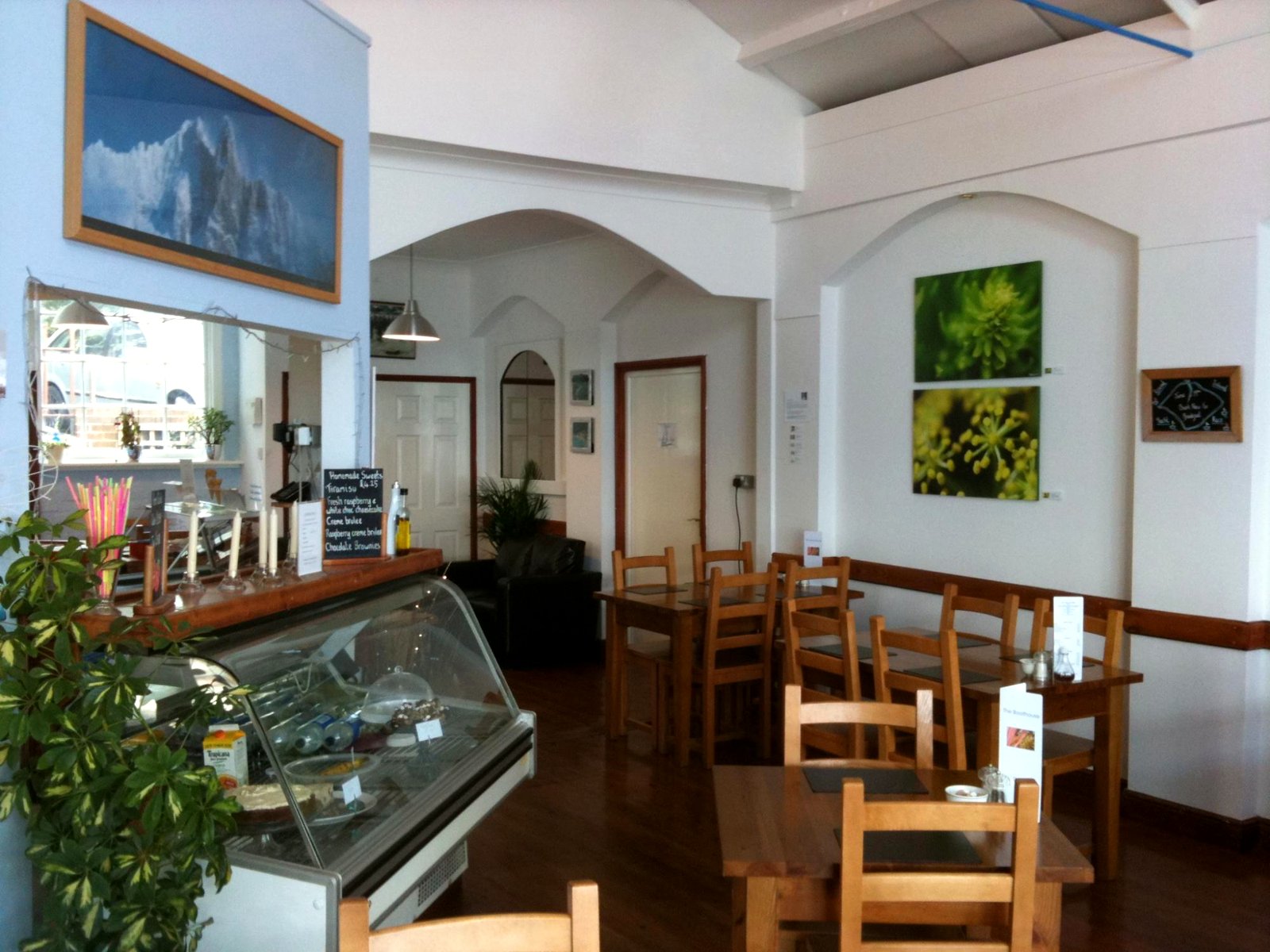 Inside the Boat House: white arches, wooden tables and chairs, and a glass cake counter by the window