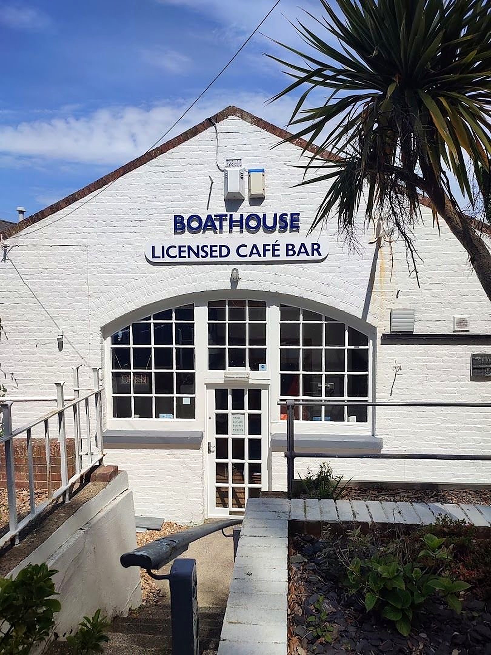 The white Boat House building with arched windows and the sign Boathouse Licensed Café Bar, under a blue sky